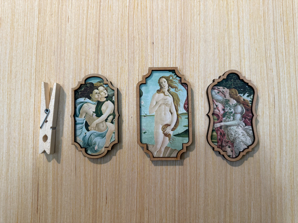 Three framed artworks on a wooden surface with a clothespin on the left.