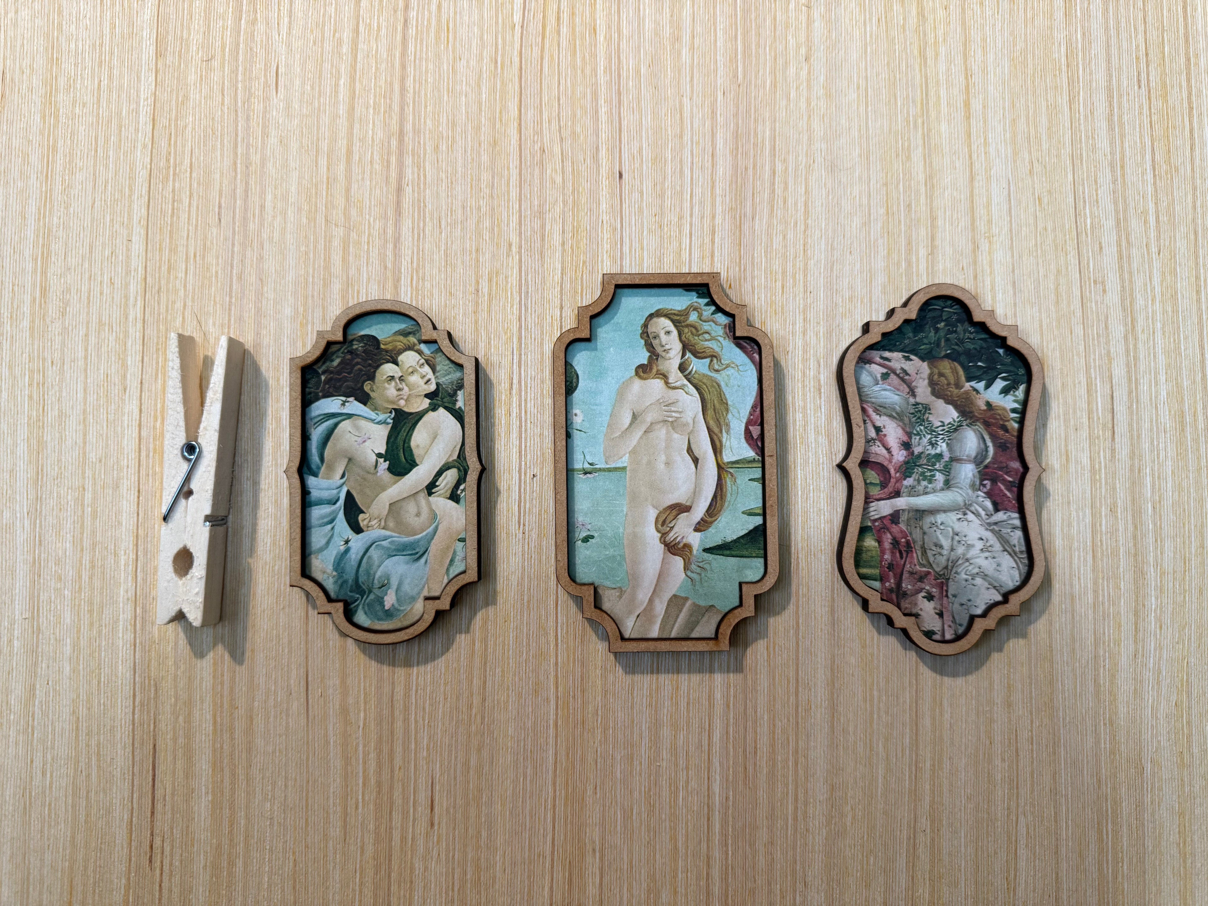 Three framed artworks on a wooden surface with a clothespin on the left.